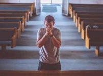 手を組んで教会で祈る男性