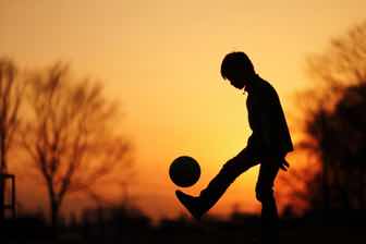 夕日を背にサッカーボールで遊ぶ少年